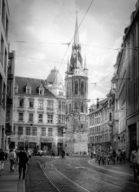 People walking on street amidst buildings in city against sky