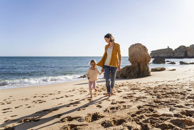 Mother with daughter walking on shore at beach