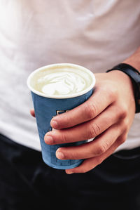 Young man holding coffee disposable paper cup in street