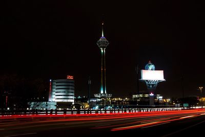 Light trails on road with milad tower against sky in city at night