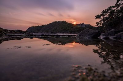 Reflection of rocks in sea against sky during sunset