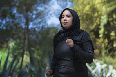 Portrait of young woman standing against trees