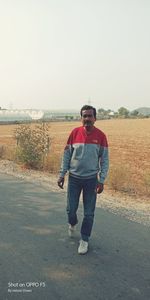 Portrait of young man standing on road against clear sky
