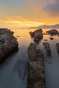 Rocks on shore against sky during sunset