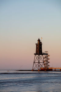 Lighthouse by sea against clear sky during sunset