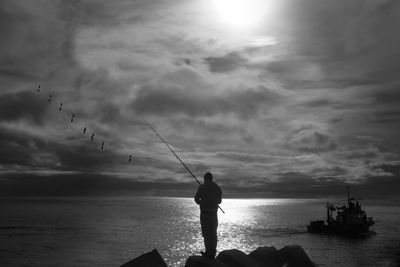 Silhouette man fishing in sea against sky during sunset