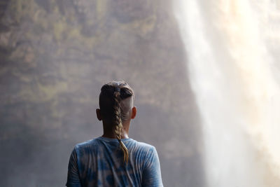 Teenager looking as waterfall cascades in front of him.