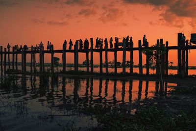 Silhouette wooden posts in sea against sky at sunset