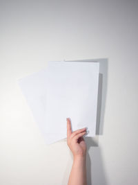 Midsection of woman holding paper against white wall