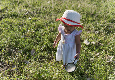 A young child is bending down looking in the grass, investigating something with a magnifying glass.