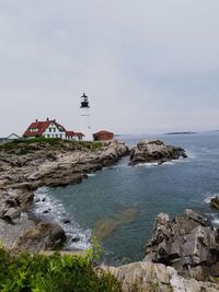 Lighthouse amidst sea and buildings against sky