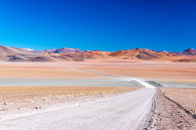 Scenic view of arid landscape against clear blue sky on sunny day