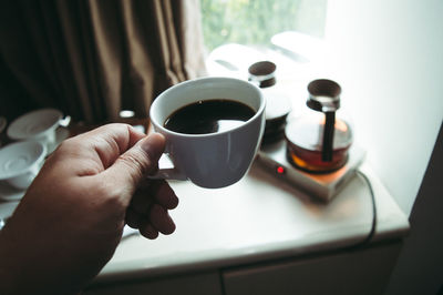 Close-up of hand holding coffee cup on table