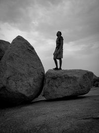 Rear view of woman standing on rock against sky