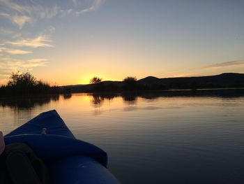 Low section of trees by lake against sky during sunset