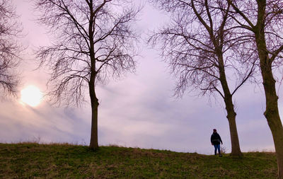 Man standing by bare trees on field against sky