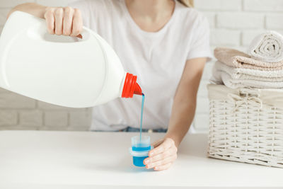 Midsection of woman holding white while standing on table at home