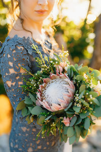 Midsection of bride holding bouquet standing outdoors