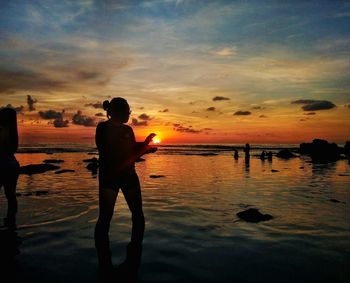 Silhouette woman standing at beach against sky during sunset