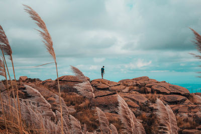 Man standing on rock by sea against sky