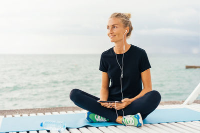 Woman resting after sports workout by the seacoast and listening to music  on headphones.