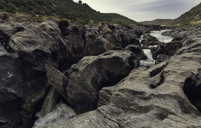 Waterfall between the rock formations on the guadiana river with the mountains and the cloudy sky