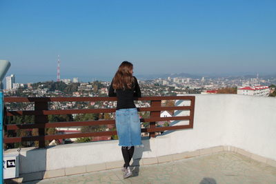 Rear view of woman looking at cityscape against clear sky