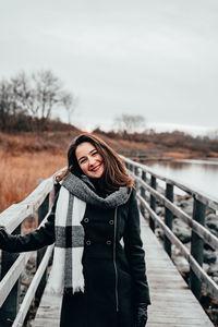 Portrait of young woman standing on footbridge against clear sky