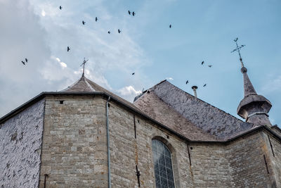 Low angle view of birds flying in old building against sky