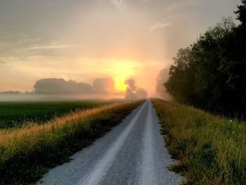 Road amidst field against sky during sunset