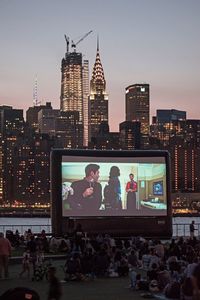 People on illuminated modern buildings in city against sky