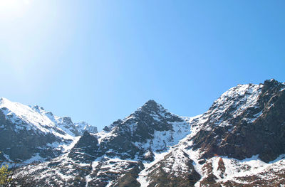 Low angle view of snowcapped mountains against clear blue sky