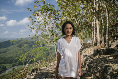 Portrait of smiling young woman standing against trees