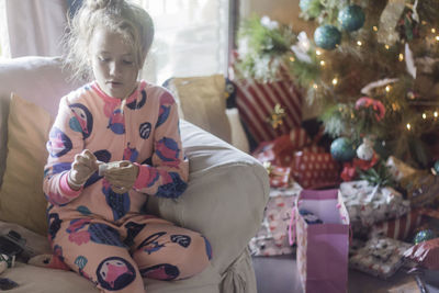 Girl reading label while sitting on sofa against christmas tree and presents