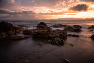 Rocks on beach against sky during sunset