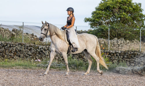 White lusitano mare, female dressage rider, outdoors on sand.