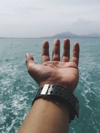 Cropped hand of man gesturing against sea