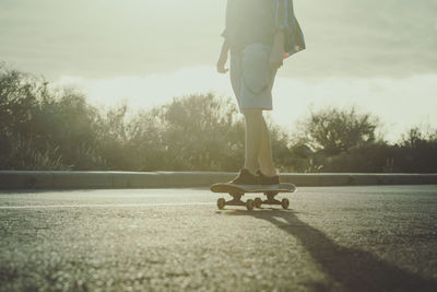 Low section of person skateboarding on street against sky during sunset