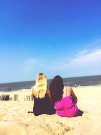 Rear view of female friends sitting at beach on sunny day
