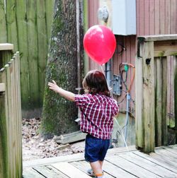 Rear view of boy holding pink balloon standing at porch
