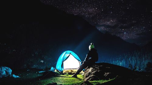 Rear view of men sitting on rock against sky at night