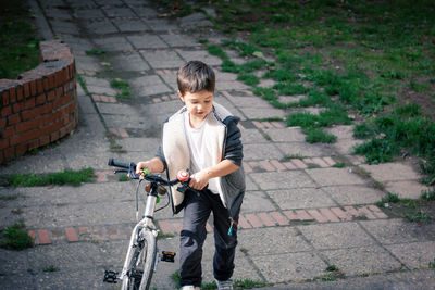 Boy walking with bicycle on footpath