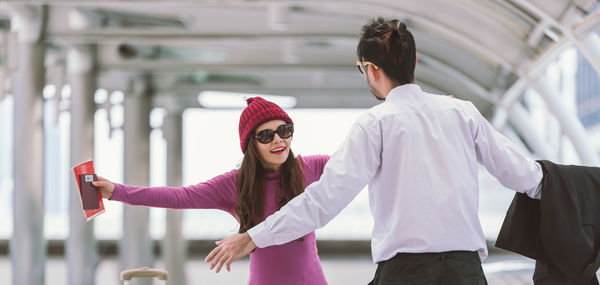 Smiling woman with boyfriend gesturing on elevated walkway at airport