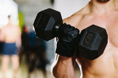 Midsection of shirtless man exercising with dumbbell in gym