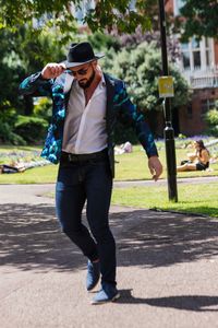 Full length of man holding hat standing on street