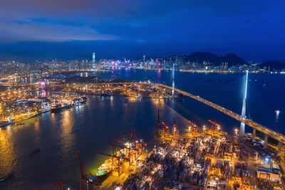 High angle view of illuminated city by sea against sky