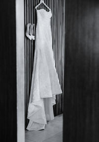 Wedding dress hanging next to shoes during the preparation of the event, black and white photo