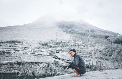 Side view of young man looking away while crouching against mountain