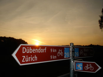 Close-up of german text sign post against sunset sky