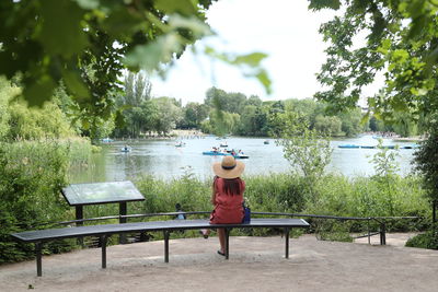 Man sitting on bench by lake against trees